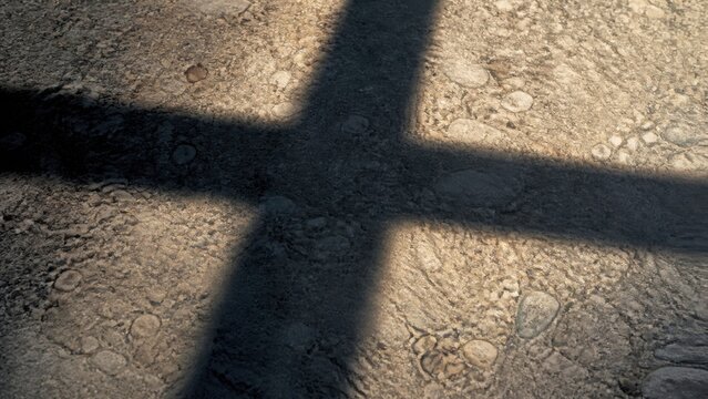 Shadow of a cross cast across rocky ground. Christian faith symbol representing crucifixion, sacrifice, forgiveness, and reflection during Good Friday and Easter.