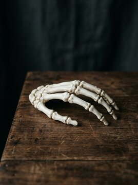 Realistic Human Skeleton Hand Resting on a Rustic Wooden Table.