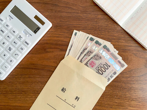 木製机の上に置いたお金の入った給料袋と電卓・通帳／家計管理イメージ