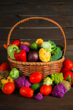 Fresh, shiny vegetables of various varieties in a wicker basket on a wooden background.