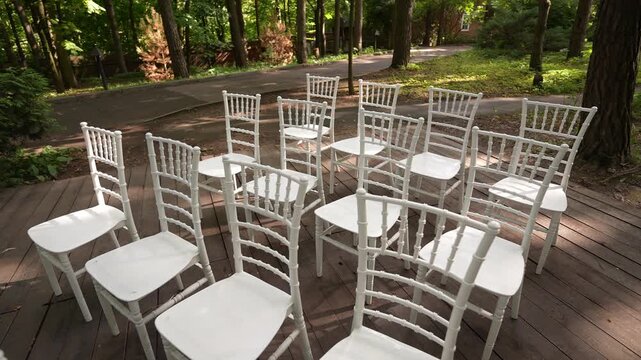 Outdoor arrangement of white Chiavari chairs on wooded deck showing empty seating cluster under dappled canopy light, with chair, white, chiavari, seating detail