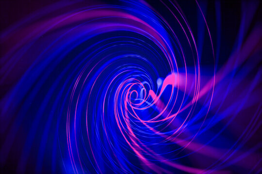 Abstract swirling vortex of blue and pink light trails on dark