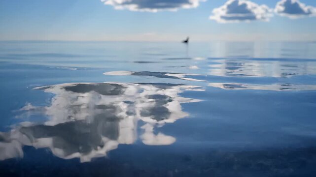 Close-up of a water surface with gentle ripples reflecting drifting clouds. Sparkling sunlight on blue water with subtle movement