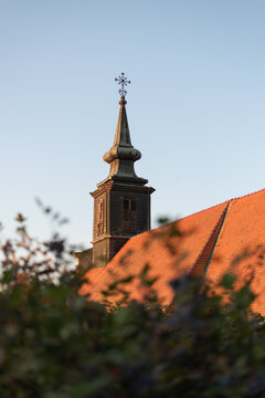 Historic Petrovaradin church steeple with metal cross rises behind red-tiled roof. Novi Sad, Serbia