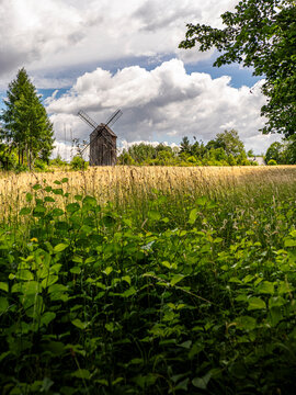 Historic Wooden Windmill Standing in Golden Field Under Dramatic Cloudy Sky in Summer Countryside