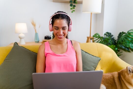 A Hispanic woman smiles while using a laptop on a yellow couch