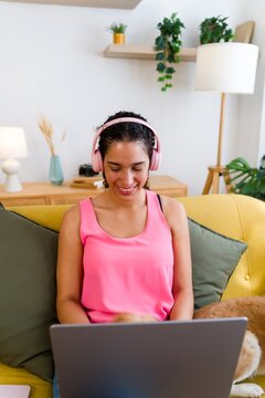 A Hispanic woman wearing pink headphones enjoys using a laptop