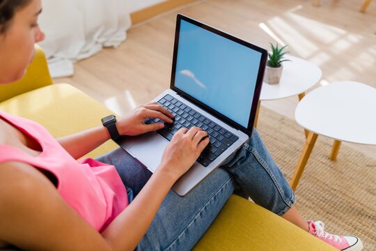 A Hispanic woman types on a laptop in a modern living room