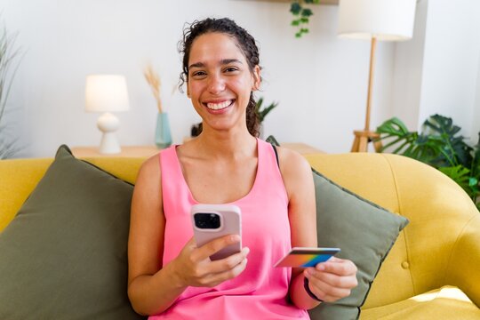 A smiling Hispanic woman uses a mobile phone and credit card