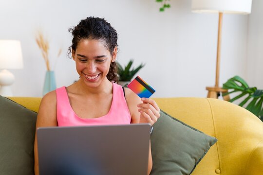A Hispanic woman happily shops online using a credit card and laptop