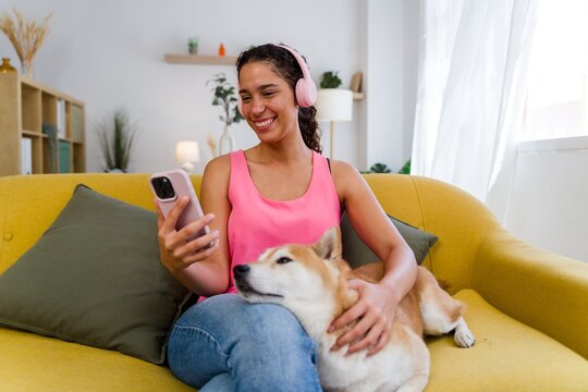 A Hispanic woman listens to music and pets her dog on a yellow couch