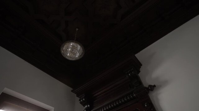 Ornate coffered ceiling with suspended crystal chandelier and carved wooden cornice in historic interior, with chandelier, crystal, ceiling, coffered detail, showing woodwork, carving, cornice