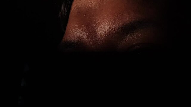 Macro close up view of an adult Indonesian male face focusing on both eyes under dramatic low key studio light capturing natural skin detail and steady gaze in the dark environment