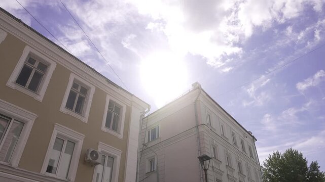 Sunny upward view of adjacent historic urban buildings with strong sun flare, with architecture, building, facade, window detail, showing stucco, trim, cornice, molding context