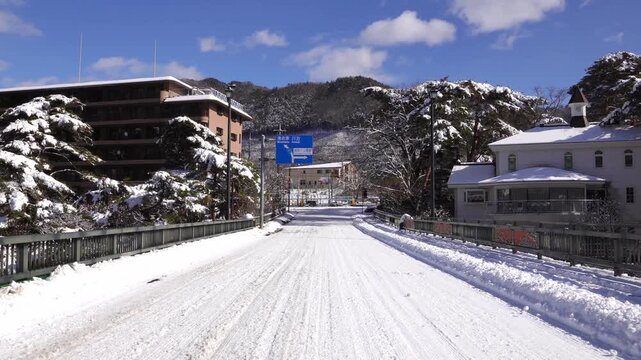 Snowy road scene with a Japanese road sign for Minamiaizu Kawaji on a sunny winter day.