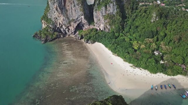 Aerial view of Railay Beach with limestone cliffs, turquoise water, and longtail boats on the sand in Ao Nang, Krabi, Thailand.