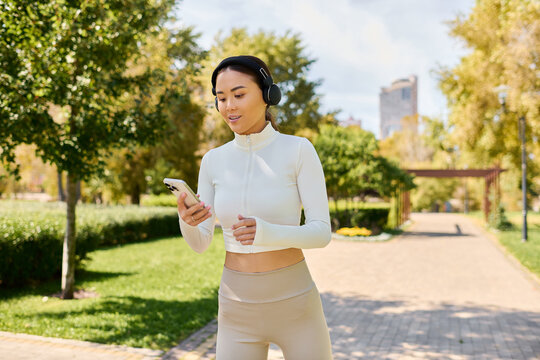 A young beautiful Asian woman listens to music while walking in a sunny green park.