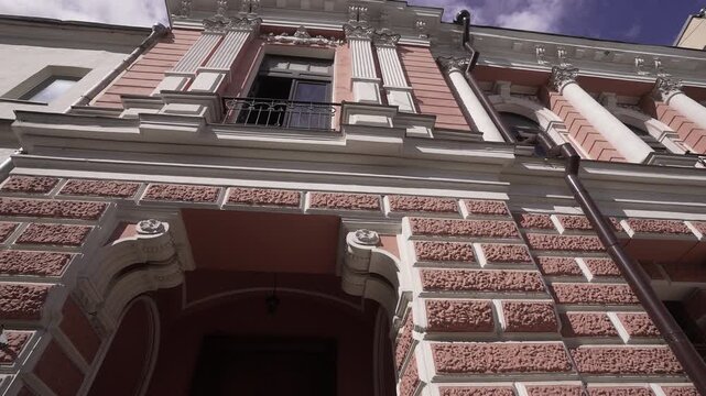 Worm's-eye view of ornate pink historic building facade with open upper window and iron balcony, with architecture, facade, historic, ornament detail, showing masonry, rusticated, pink, plaster