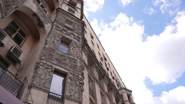 Low‑angle tilt of ornate historic building facade with carved stone reliefs and balconies against partly cloudy sky, with architecture, facade, ornament, stone detail