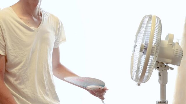 扇風機の風に当たりながらうちわを扇ぐ暑がりの男性