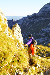 Fototapeta premium Hiker gripping fixed steel cable ascending steep trail near limestone cliffs in Durmitor. Depicts protected scrambling techniques, extreme route adventure, and alpine safety equipment practice.