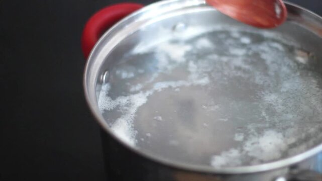 Skimming foam from boiling broth in saucepan with wooden spoon