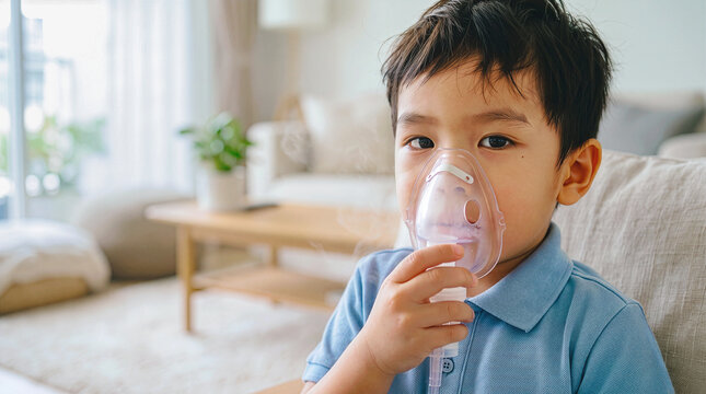 Little asian boy inhaling asthma medicine using nebulizer mask for respiratory treatment at home