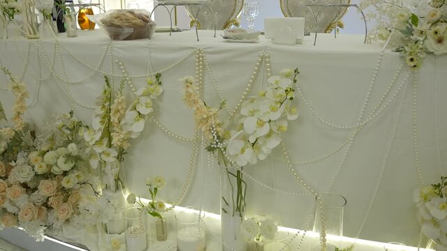 Elegant wedding head table with pearl swags and cascading orchid and rose arrangements under warm accent lighting, with wedding, headtable, reception, banquet detail