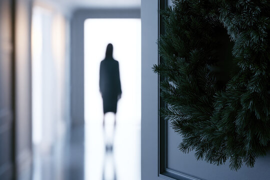 Dark evergreen wreath mockup conceptual stock photography with sharp pine foreground, blurred human silhouette bright hallway, minimalist charcoal door, soft morning daylight, Scandinavian