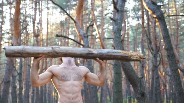 Muscular man lifting hard weight over head training hands. Strong guy with naked torso working out in forest. Athlete exercising at beautiful nature environment. Sport and active lifestyle. Close up