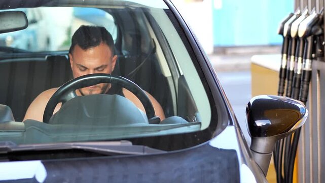 Focused young man sitting in the driver's seat of a car at a gas station