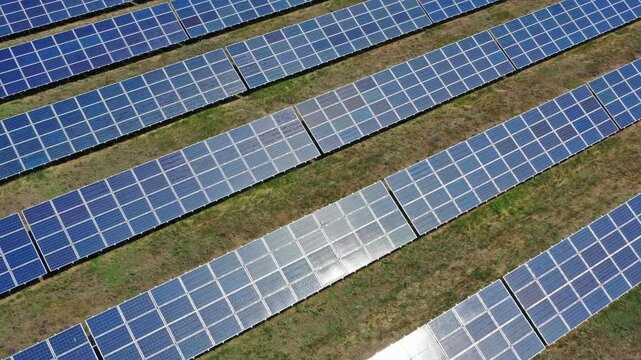 Aerial view of rows of photovoltaic solar panels installed in a grassy field, capturing sunlight reflection across the energy farm in Russia.