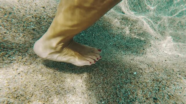 V&iacute;deo submarino art&iacute;stico de un pie sobre arena bajo agua transparente con reflejos solares.