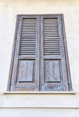 Fototapeta premium Closed dark brown wooden shutters on a traditional Mediterranean building facade in Sicily, Italy, showing rustic architecture, aged texture and classic louvered design.