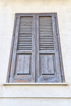 Closed dark brown wooden shutters on a traditional Mediterranean building facade in Sicily, Italy, showing rustic architecture, aged texture and classic louvered design.