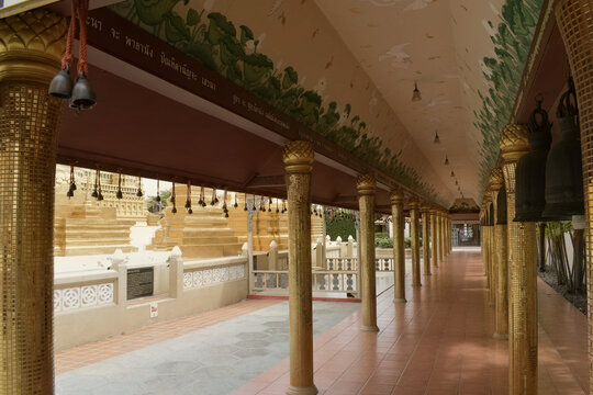 oriental temple cloister walkway lined with shimmering gold mosaic tiled pillars traditional hanging bronze bells and floral lotus ceiling artwork