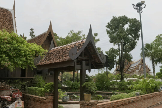 scenic garden landscape of a traditional oriental wooden house featuring an ornate timber entrance gate tiled roofs water pond and lush tropical trees