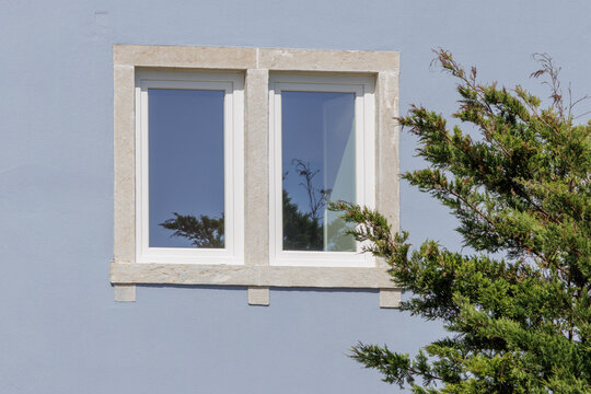 Building window with stone frame reflecting sky and green tree