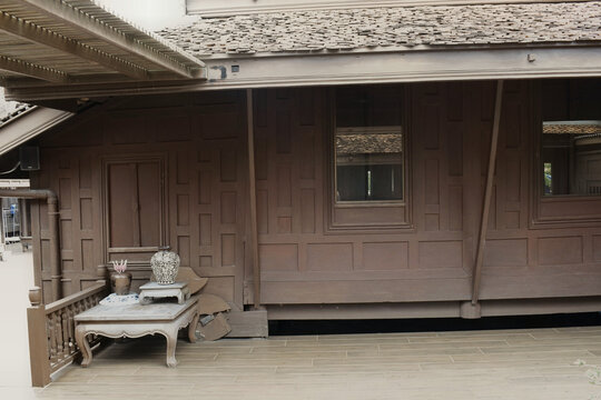 authentic teak wood paneled facade and tiled roof of an oriental heritage house with antique ceramic vases resting on a low wooden table on the open terrace