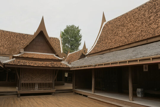 traditional oriental teak house compound featuring raised wooden terrace deck intricate lattice carvings and curved clay tiled gabled roofs