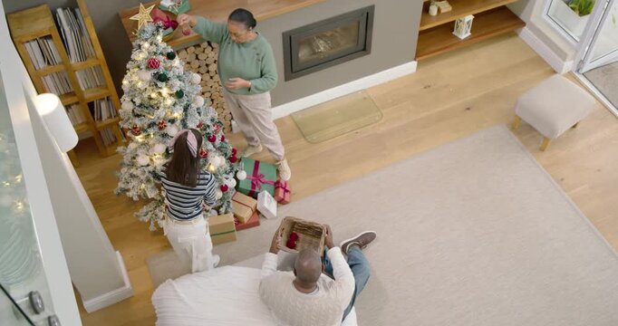 Family decorating flocked tree for Xmas at home, man with basket handing ornaments, copy space