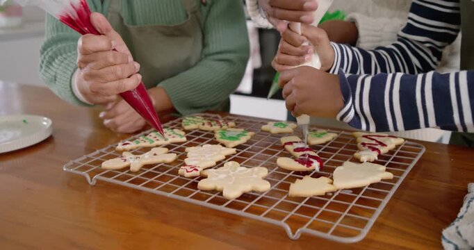 Piping bags are entering as adult is guiding while child is decorating holiday cookies on table