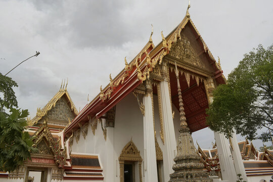 low angle exterior view of the ornate golden carved gables and multi tiered roof of 'phra ubosot ordination hall' at 'wat pho', bangkok, thailand