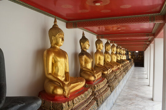 vanishing perspective of seated golden buddha statues lining the marble cloister corridor at wat pho inin bangkok thailand
