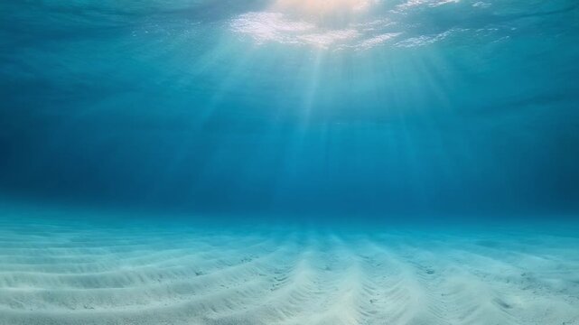 Sunlight beams through clear ocean water onto sandy seabed with gentle ripples