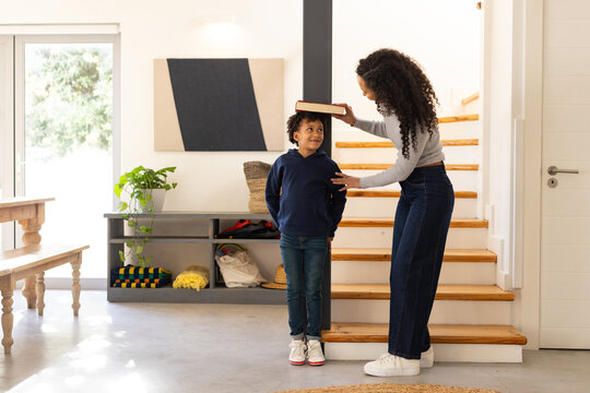 African American female mother and daughter measuring height with closed book in foyer by staircase