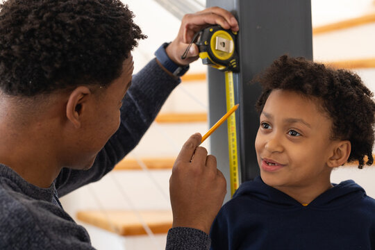 African American man and child measuring post on stair, holding yellow tape pencil, child watching