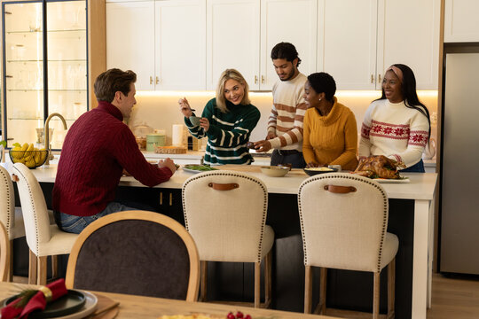 Diverse friends preparing and serving meal at kitchen island holding roasted turkey and utensils