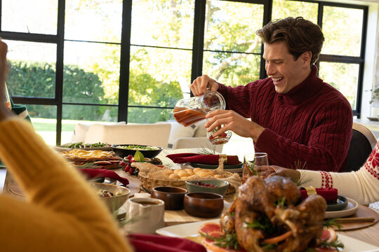 Man in burgundy sweater pouring beverage from pitcher by roasted turkey at dining table, copy space