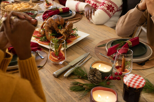 African American family sharing holiday meal at dining table, wearing knit sweaters, passing turkey